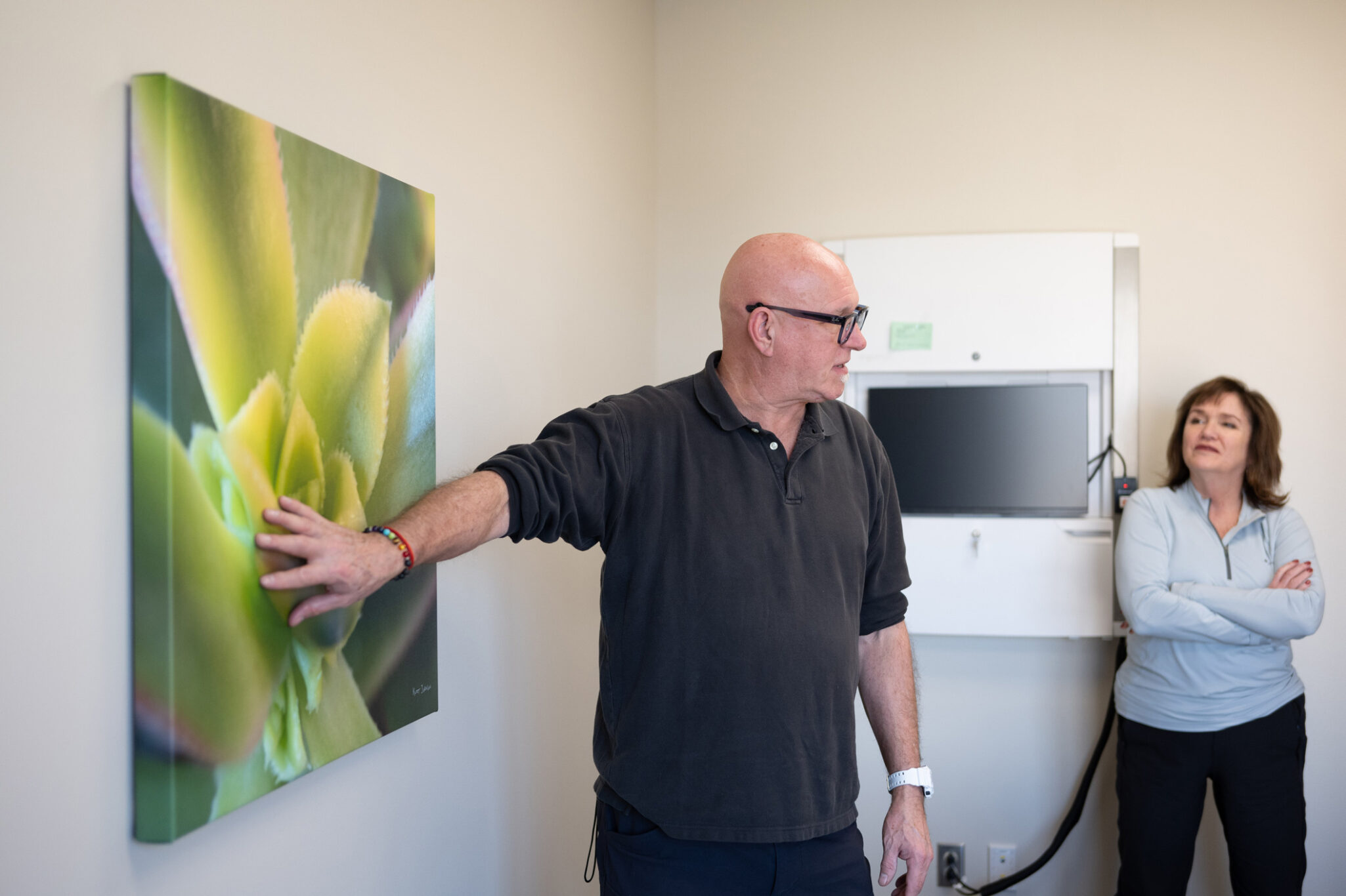 Nature photographer for healthcare with hand on gallery wrapped canvas of a green succulent, explaining the benefits of biophilic design in a patient room in a healthcare facility at Allina Health in Minnesota. 